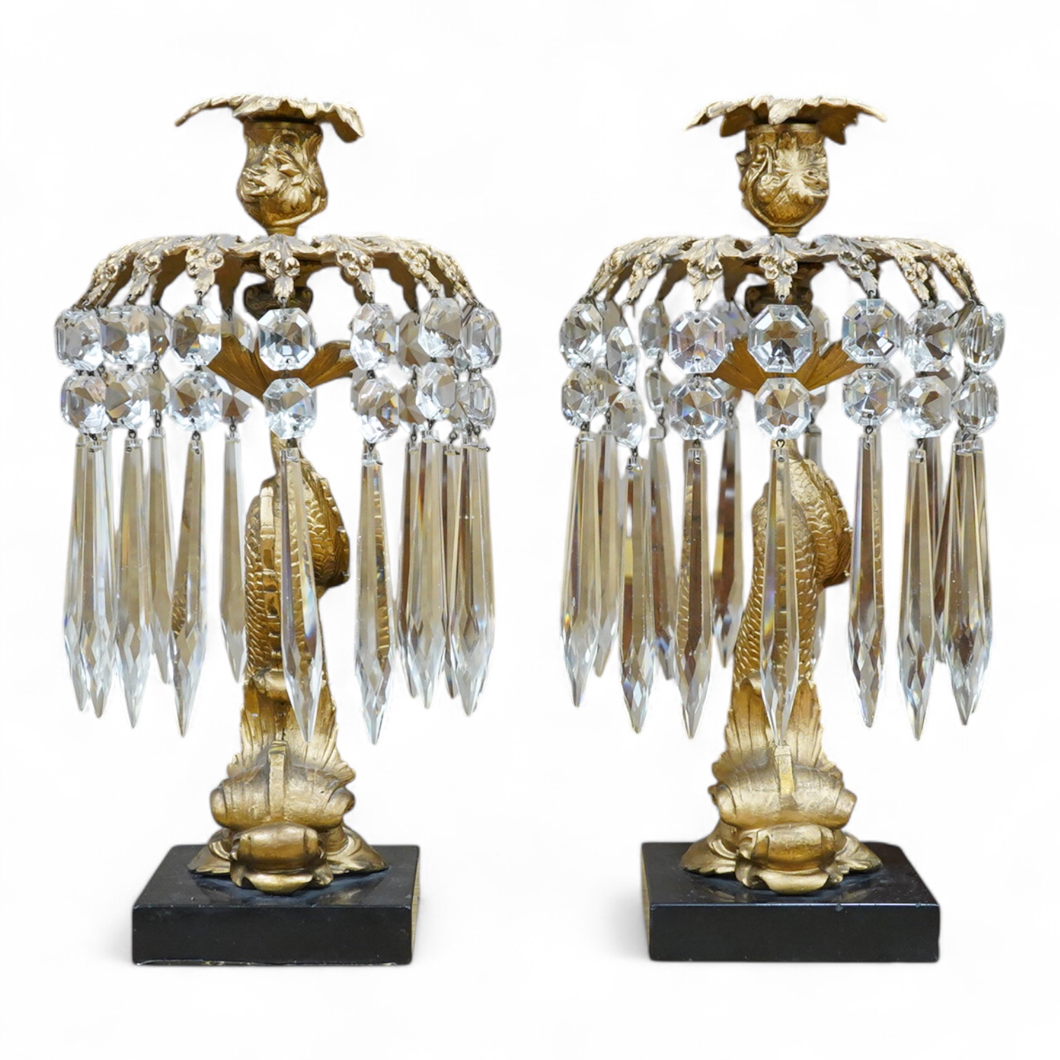 A pair of William IV gilt metal candlesticks, the stems formed as dolphins, with glass lustre drops, raised on square slate bases, 37cm high